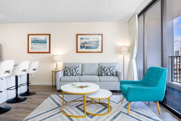 Modern living area with a gray sofa, turquoise armchair, and large windows offering city views.