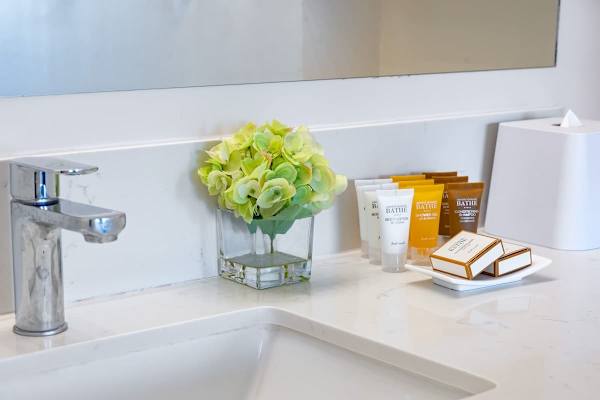 Modern bathroom countertop with complimentary toiletries and fresh floral arrangement.