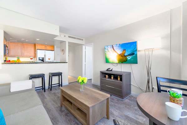 Living room with dining table for up to two people and countertop with 2 bar stools, and a flatscreen TV. 