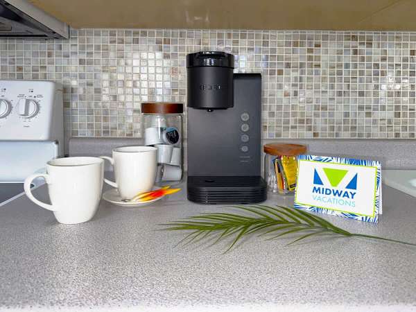 A welcoming kitchen counter setup featuring a Keurig coffee maker, two white mugs, and a jar of coffee pods, all set against a stylish mosaic tile backsplash.