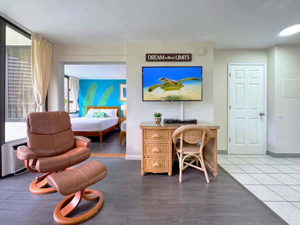 Relax in your living area featuring a comfy leather recliner and a wicker desk area perfect for working, all while having a clear view into the bright, tropical-themed bedroom!