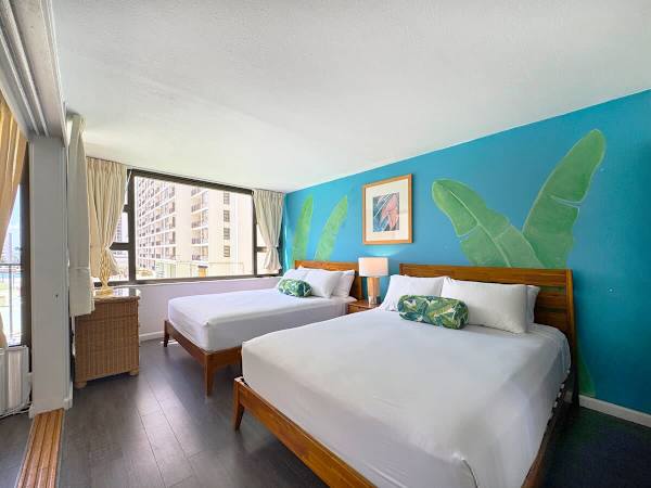 A bright, modern bedroom featuring 2 comfy queen beds and a fun, tropical accent wall painted with large banana leaves, all set up with a great high-rise view outside the window!