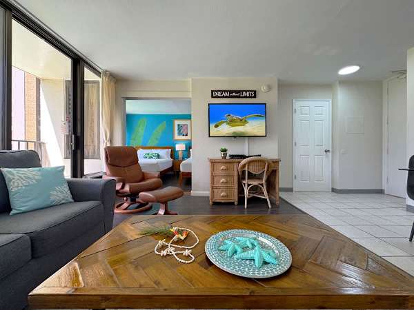 A stylish open-concept living area showcasing a beautiful wooden coffee table, a comfortable recliner, and a direct view into the bright, tropical bedroom.