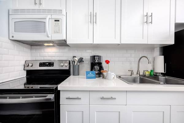 Prepare meals with ease in this well-equipped kitchen featuring gleaming white cabinetry, modern appliances including a GE microwave and electric range, and essential small appliances like a coffee maker.