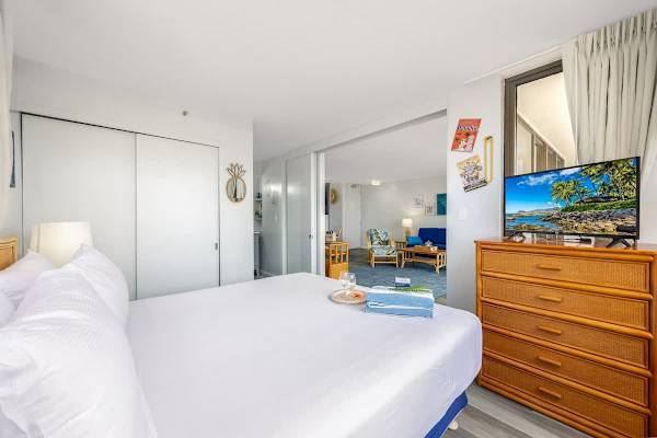 The bedroom offers a king-size bed, ample closet space, a 32" flat-screen TV with Roku, and seamless access to the bright and stylish living area beyond.