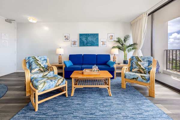 Step into our vibrant and comfortable living room, featuring stylish tropical decor, a blue pull-out sleeper sofa, and direct access to your private balcony for a truly relaxing escape.