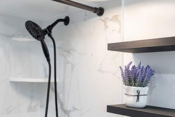 A modern bathroom, featuring a stylish black shower head, a white marble-patterned wall, and decorative shelving.