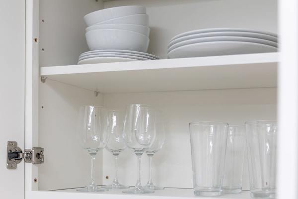A cabinet stocked with clean white bowls, plates, and a variety of glassware.
