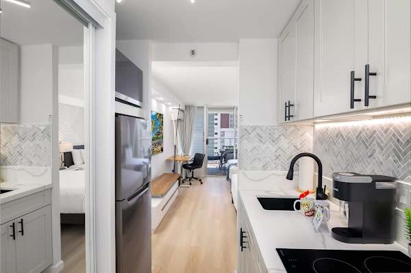 A compact and well-designed studio apartment with a modern galley kitchenette, a cozy sleeping area, and a bright living space.