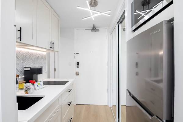 A sleek, modern kitchenette with a refrigerator and a coffee station, featuring a stylish herringbone tile backsplash.