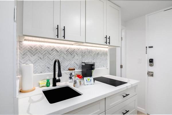 A fully-equipped kitchenette featuring a modern black sink and faucet, a coffee station, and a stylish herringbone tile backsplash.