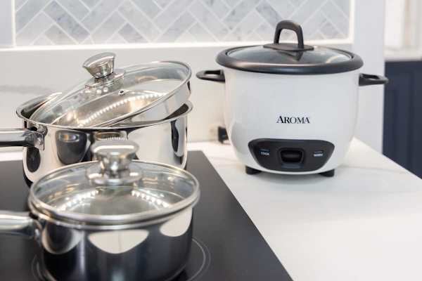 A well-stocked kitchenette, highlighting a rice cooker and a set of stainless steel pots and pans.