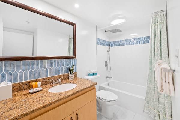 Full bathroom that features a granite vanity, a stylish blue tile backsplash, and a clean tub/shower combo.