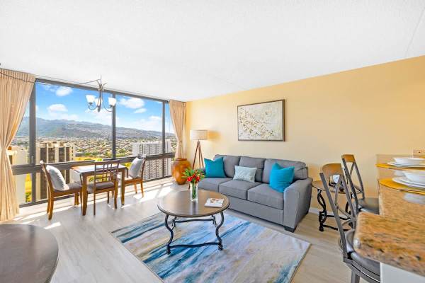 The living area features a pull-out sleeper sofa, a dining space, and floor-to-ceiling windows showcasing expansive city and mountain views.
