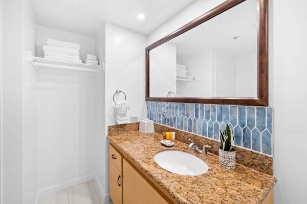 The stylish vanity features a granite countertop, a bold blue tile backsplash, a large mirror, and open shelving for easy access to towels and storage.