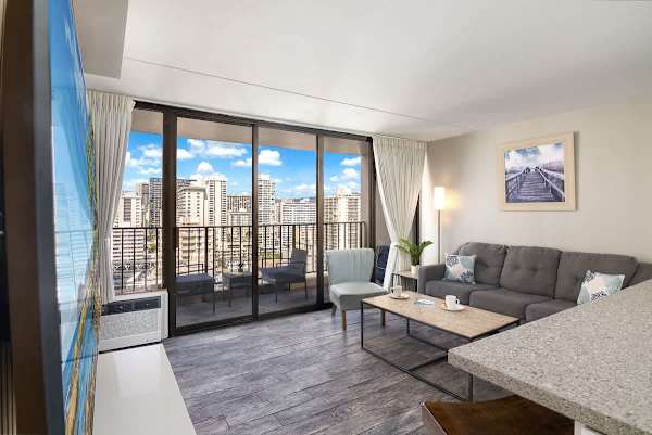 The living area features a cozy pull-out sleeper sofa, access to the balcony, and a stylish media center with a mounted 65" Smart TV.