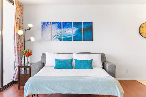 Modern living room with a pull-out sofa bed and ocean wave artwork.