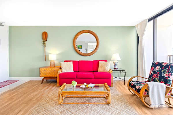 Relax in your vibrantly decorated living space with a bright magenta sleeper sofa, tropical rattan furniture, and stylish wall decor.