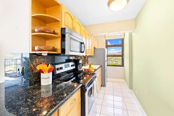 The full, well-equipped kitchen features granite countertops, warm wood cabinetry, and a window offering a glimpse of the scenic view.