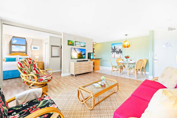 This unit features a vibrant tropical aesthetic with rattan furniture, a dedicated dining area, and a bedroom separated by a sliding door.