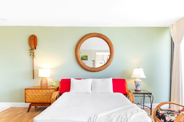 The pull-out sleeper sofa provides a comfortable bed, framed by charming tropical decor, including a large round mirror and unique wooden accents.