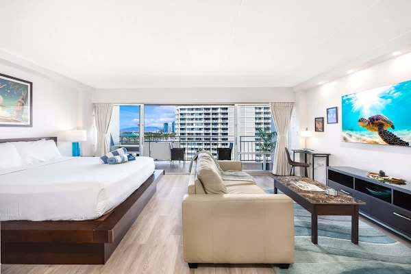 Your studio features a king-size bed, a side table, and easy access to the balcony with stunning harbor and ocean views through the wide sliding glass door.