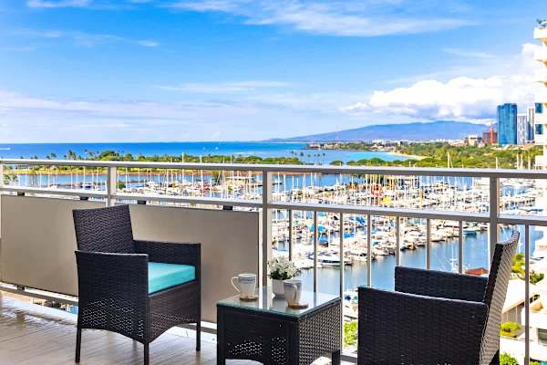 Enjoy a stunning panoramic view of the sparkling harbor, marina, and ocean from a private balcony with comfortable outdoor seating.