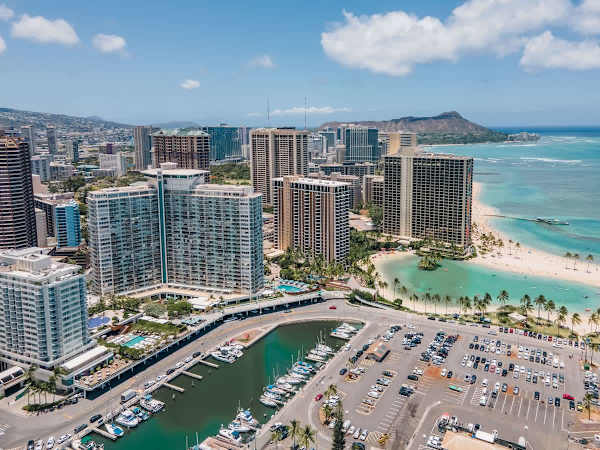 A stunning aerial view showcasing the Ilikai Hotel in the heart of Waikiki, highlighted against the city skyline and lush mountains.