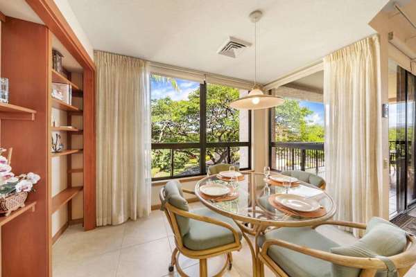 Sunlit dining area features table, chairs, artwork, windows, and kitchen