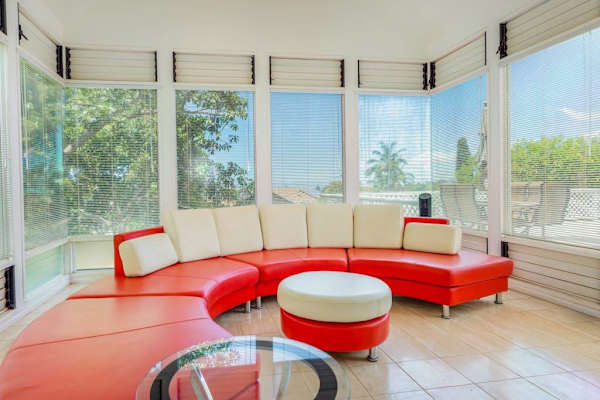 Sunlit lounge features curved seating, windows, artwork, and tropical greenery