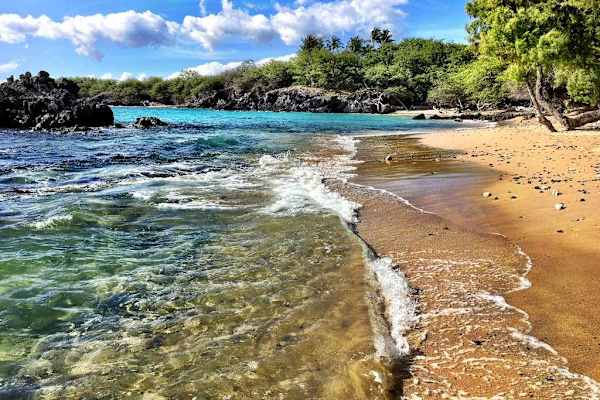 Turquoise waters crashing on to the white sandy beaches with views of the lush tropical trees.