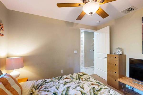 Guest bedroom with queen bed, flat screen tv and a ceiling fan.