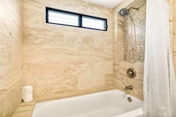 A full bathtub and shower combination in the primary bathroom, accented by elegant stone tiling