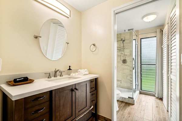 A bright and modern bathroom featuring a spacious vanity, round mirror, and a glass-enclosed walk-in shower
