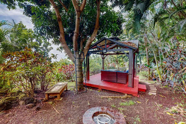 Red garden bench offers shaded seating beneath mature tropical trees