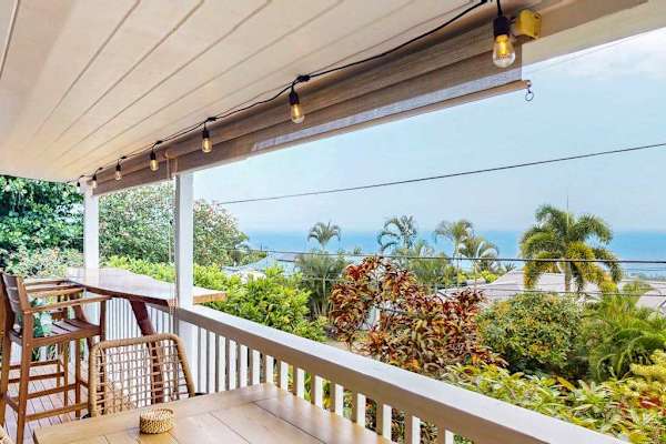 Covered balcony opens toward tropical landscaping and broad ocean scenery