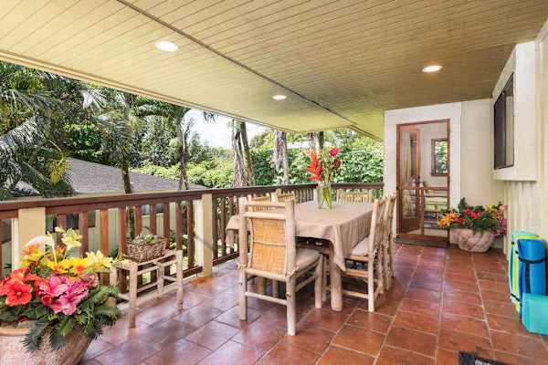 Covered patio features outdoor dining, tropical flowers, and scenic greenery