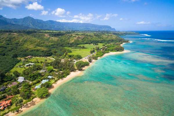 Aerial coastline reveals turquoise waters, sandy beaches, and lush valleys
