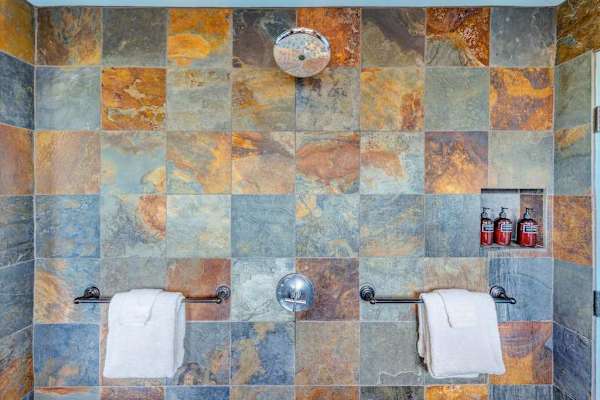 Stone-tiled spacious shower featuring necessities