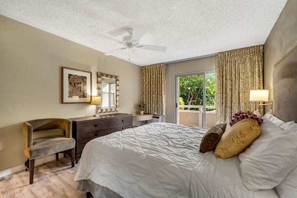 Alternate Angle of Primary Bedroom Highlighting Wooden Dresser, Accent Chair, and Balcony View