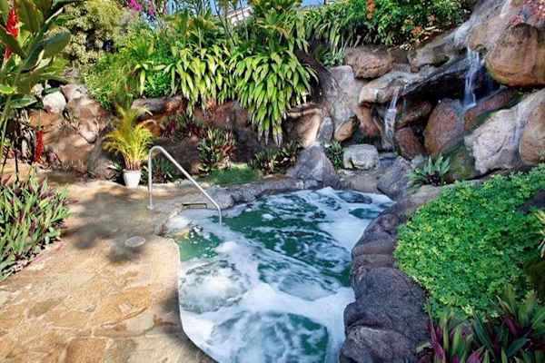 Spa hot tub nestles among rocks greenery and cascading water