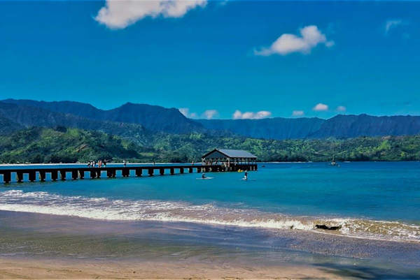 Wooden pier reaches across turquoise bay toward dramatic mountain ridges