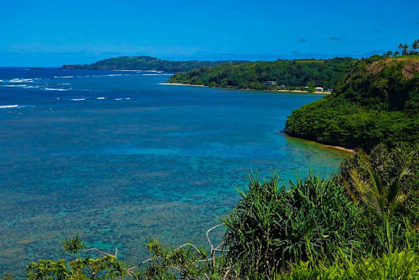 Turquoise bay unfolds beyond lush cliffs beneath cloudless island horizon