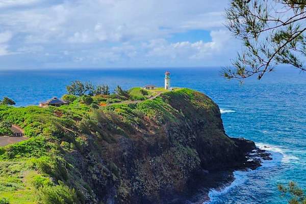 Clifftop greenery frames blue ocean and distant lighthouse under clouds