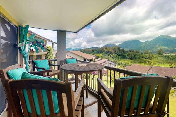 Balcony chairs overlook dramatic mountains beyond peaceful tropical resort today
