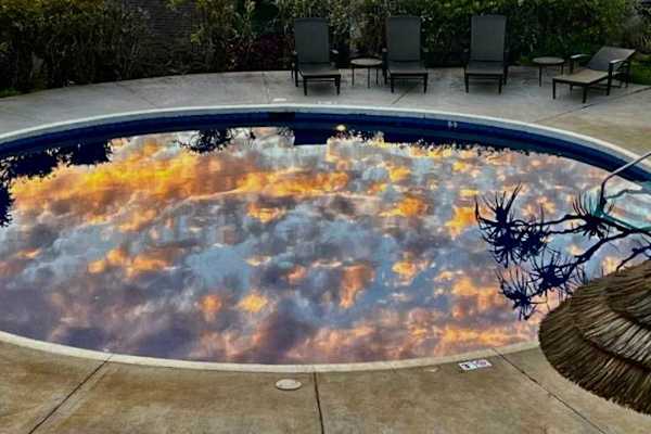 Sunset clouds reflect across circular hot tub beside quiet lounge chairs
