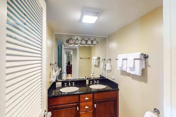 Bathroom vanity includes double sinks, mirrored storage, towels, and accessories