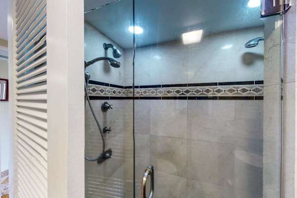 Walk-in shower features glass doors, tiled walls, and grab bars