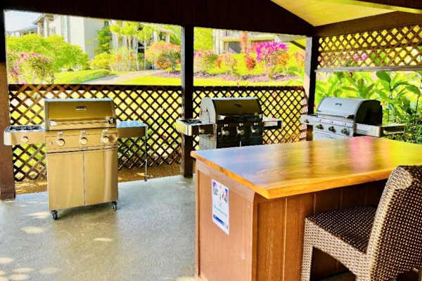 Covered outdoor kitchen includes grills, counter space, and bar seating