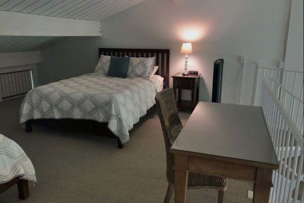 Loft bedroom includes comfortable bedding, desk, chairs, and soft carpeting